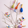 Colorful bird-shaped decorations on a branch against a light background