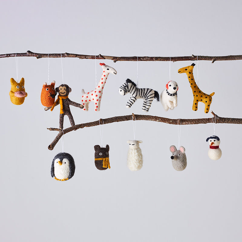 Felt animal toys hanging from a branch against a light gray background