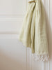 Light green towel with white fringes draped over a white door.