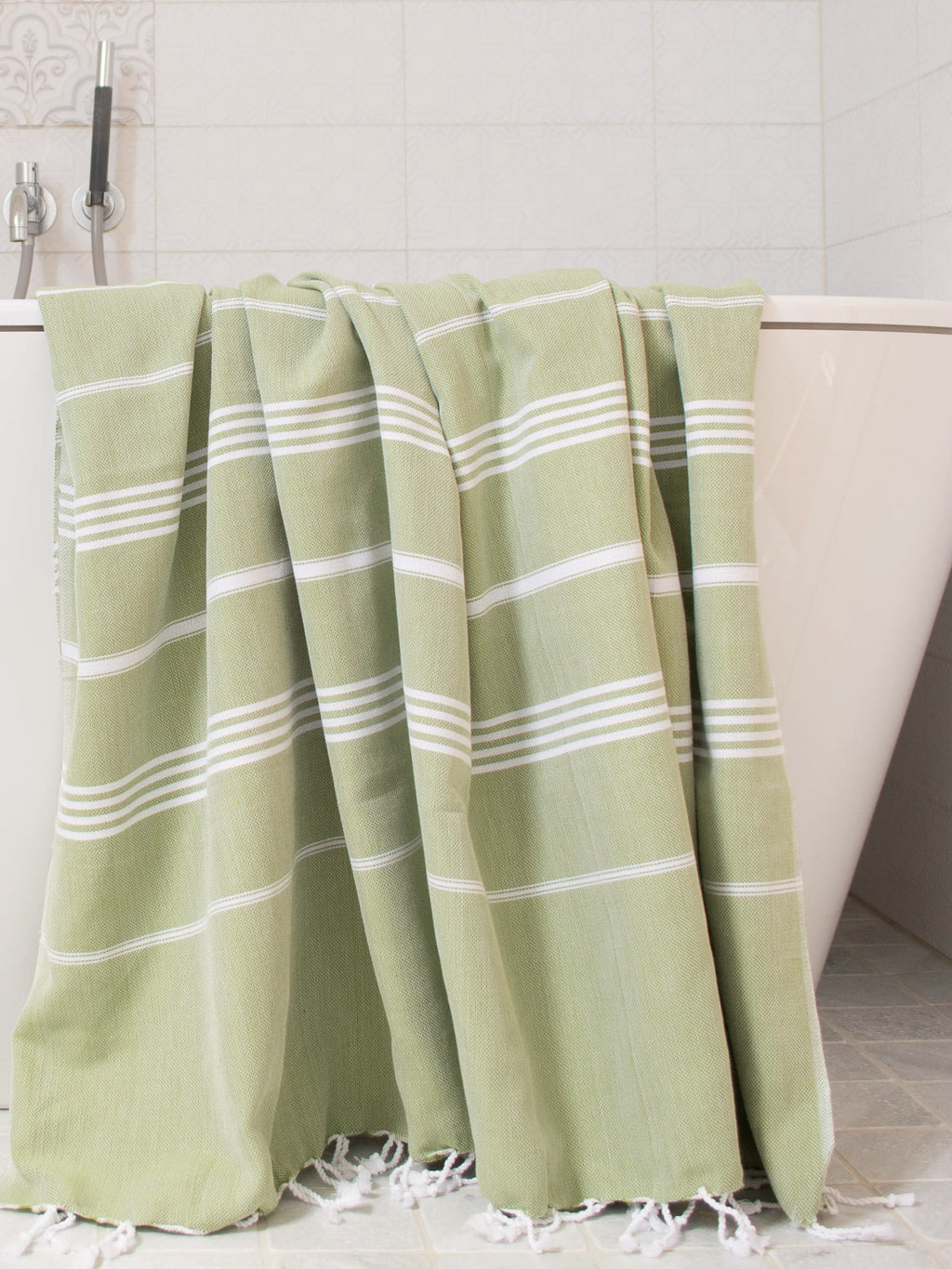 Green towel with white stripes draped over a bathtub in a bathroom setting.