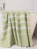 Green towel with white stripes draped over a bathtub in a bathroom setting.