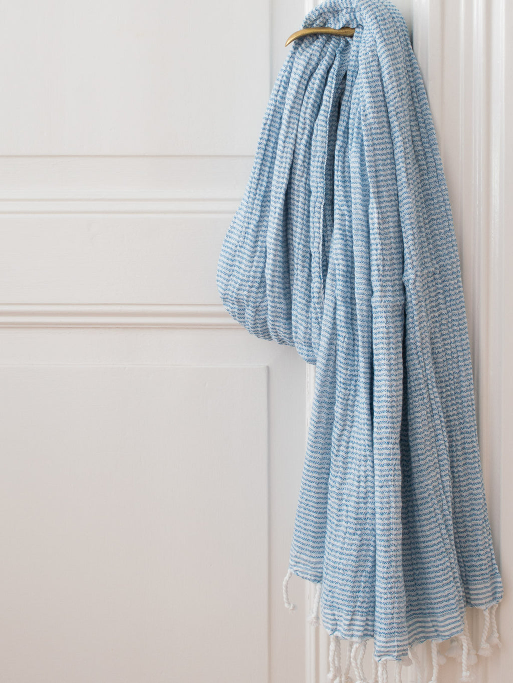 blue and white striped towel with fringes hanging on a brass door knob on a white door