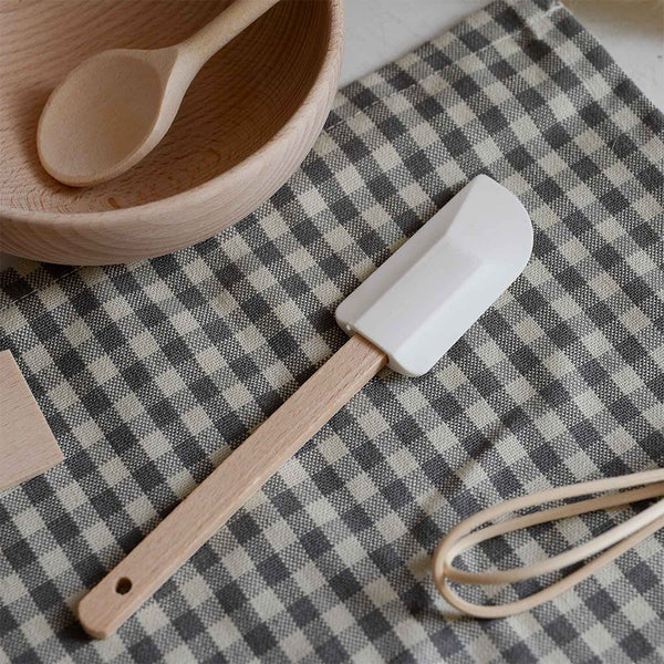 White spatula with wooden handle on a checkered tablecloth with wooden bowl and spoon.