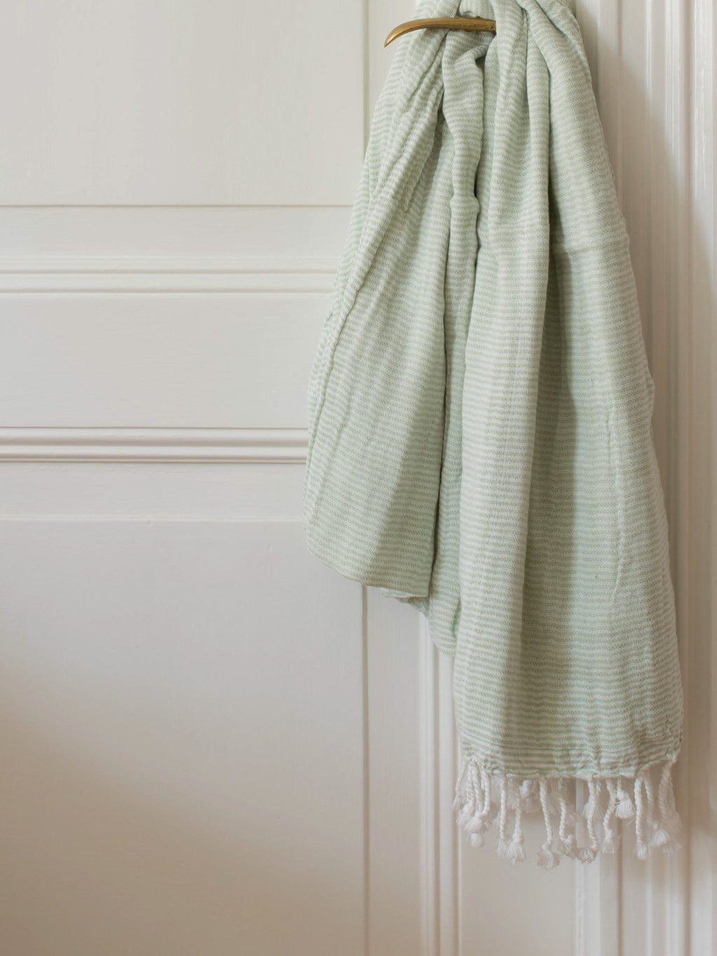 greenand white striped towel with fringes hanging on a brass door knob on a white door