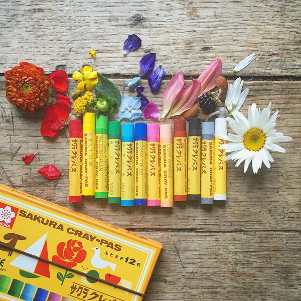 Set of Sakura Cray-Pas crayons with flowers on a wooden surface