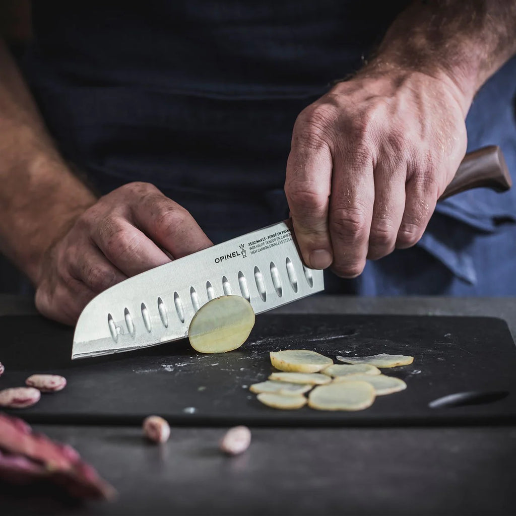 Person slicing potatoes with a Opinel knife on a dark surface