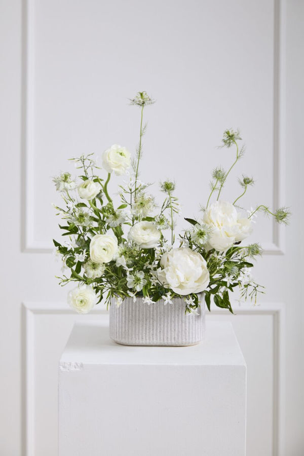 Floral arrangement in a white vase on a white surface with a light gray paneled wall background