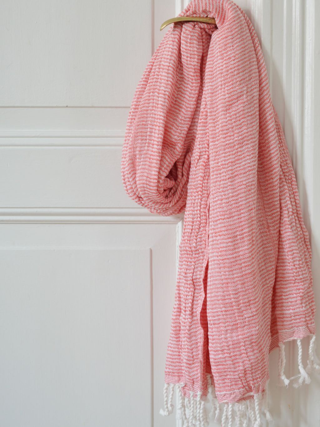 Pink and white striped towel with fringes hanging on a brass door knob on a white door
