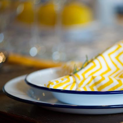 Yellow and white zigzag-patterned napkin on a white plate with blue rim, blurred background