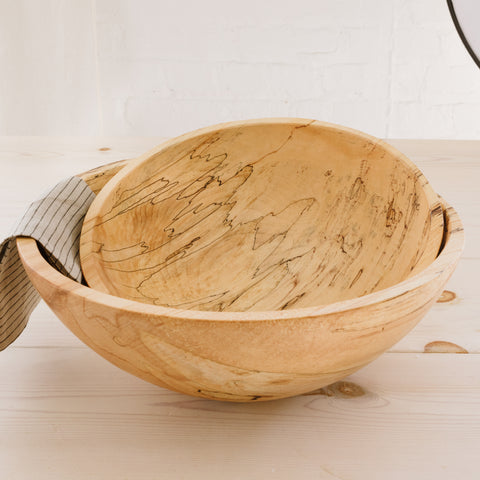 Two large spalted maple wood bowls stacked on a white surface with a striped towel to the side.