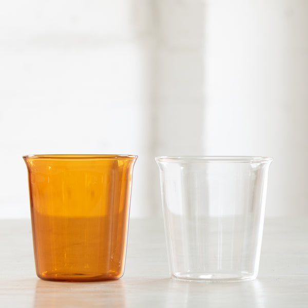 Two medium drinking glasses, one amber and one clear.